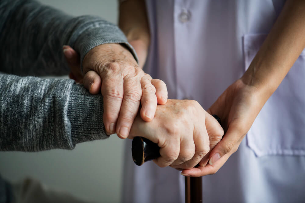 A caregiver gently supports a senior's hands resting on a cane